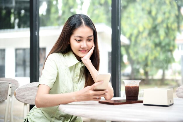 Mujer asiática con café en la mesa con un teléfono móvil en la cafetería.