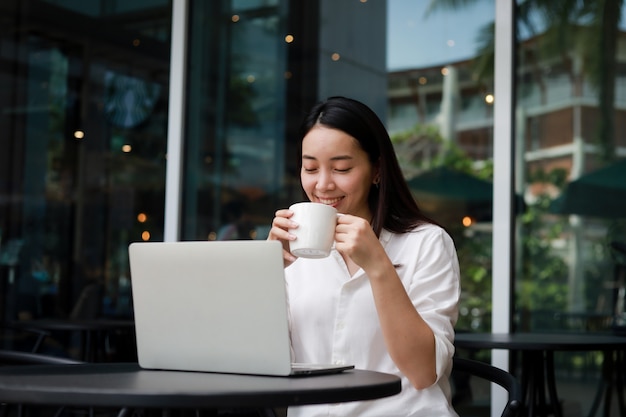 Foto mujer asiática en un café trabajando en una computadora portátil