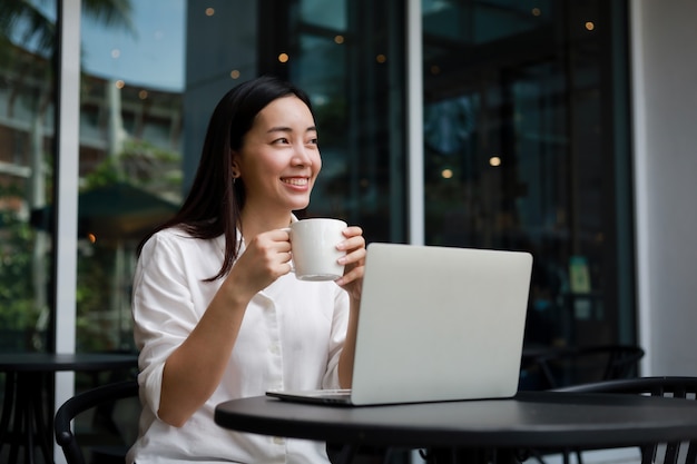 Foto mujer asiática en un café trabajando en una computadora portátil