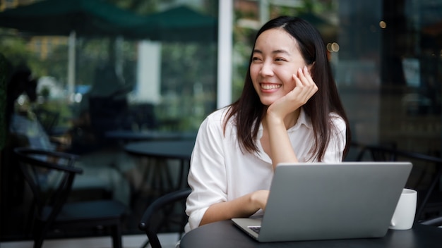 Foto mujer asiática en un café trabajando en una computadora portátil