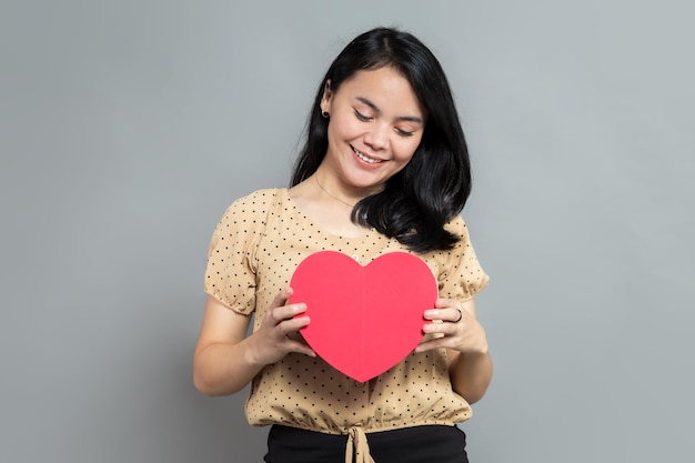 Mujer asiática con caja de regalo en forma de corazón con ambas manos