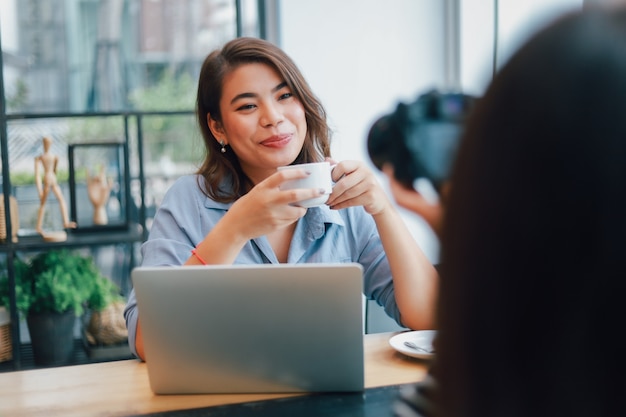 Mujer asiática en camisa azul en la cafetería tomando café y hablando con una sonrisa de novio y cara feliz