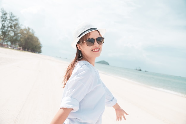 Mujer asiática con la camisa blanca que se relaja en la playa, tiempo de verano