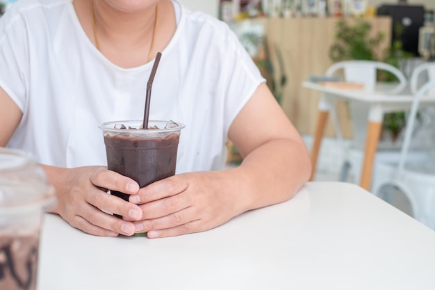 Mujer asiática con camisa blanca sentada en una mesa de madera blanca sosteniendo una taza de café en el espacio de copia de la cafetería Concepto de tiempo de relajación