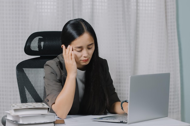 Mujer asiática cansada mientras trabajaba en una laptop en su oficina.
