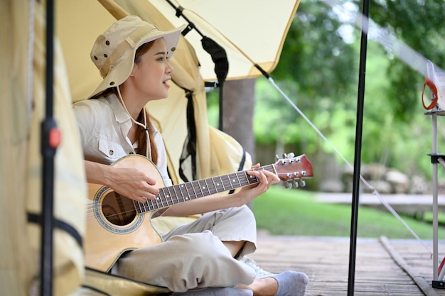 Mujer asiática canta una canción mientras toca la guitarra en su tienda de campaña mínima Concepto de camping