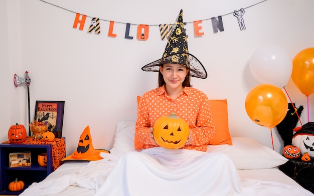 Mujer asiática con cara de calabaza para el festival de Halloween en casa. Decoración de dormitorio para celebración infantil y familiar en otoño y otoño.