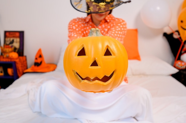 Mujer asiática con cara de calabaza para el festival de Halloween en casa. Decoración de dormitorio para celebración infantil y familiar en otoño y otoño.