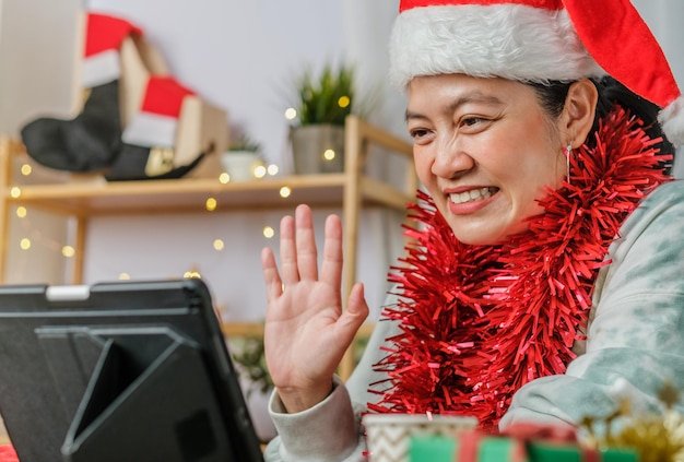 Mujer asiática celebra la fiesta de Navidad y año nuevo con amigos de videollamadas de tableta en casa