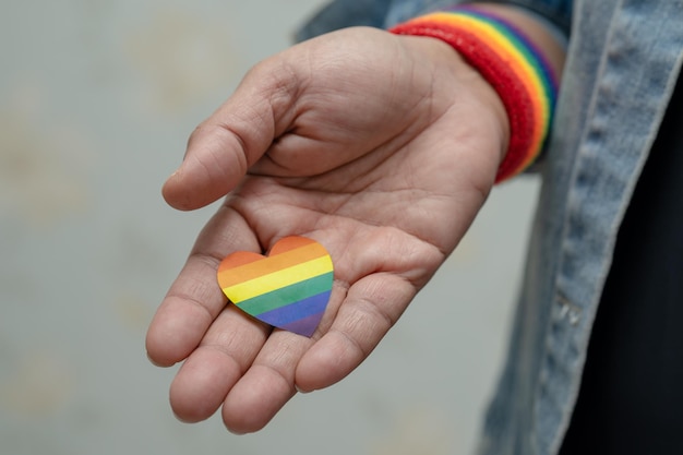 Mujer asiática con chaqueta de mezclilla azul o camisa de mezclilla y sosteniendo la bandera del color del arco iris, símbolo del corazón del mes del orgullo LGBT, celebra anualmente en junio social de los derechos humanos gay, lesbiana, bisexual y transgénero