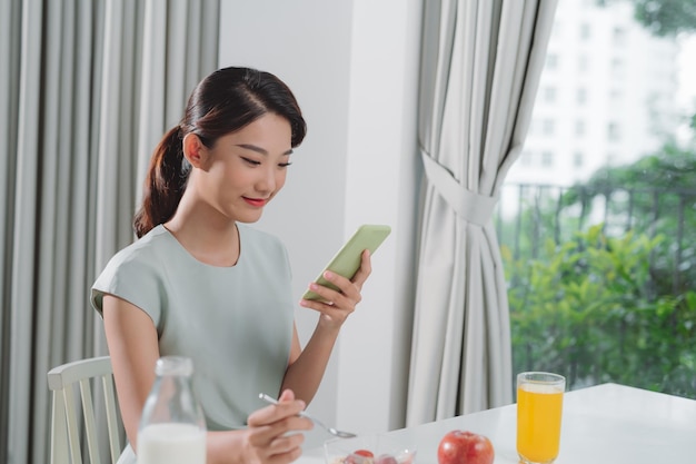 Una mujer asiática comiendo y distraída por las redes sociales.