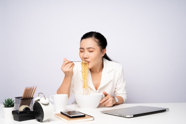 Mujer asiática comiendo fideos instantáneos después del trabajo horas extras en la oficina. Empresaria feliz con fideos después de terminar con el trabajo.