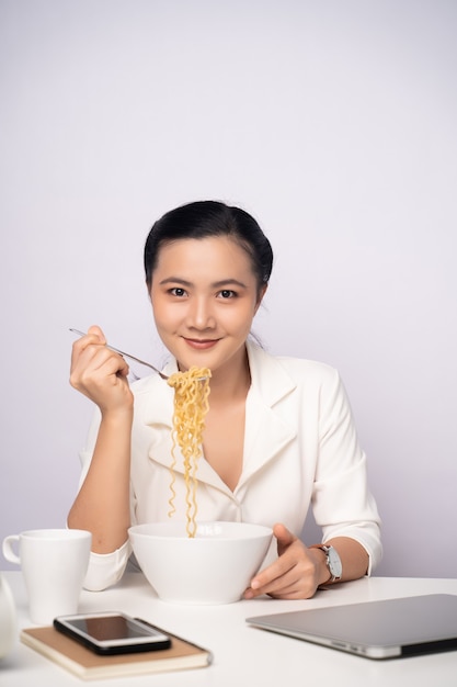 Mujer asiática comiendo fideos instantáneos después del trabajo horas extras en la oficina. Empresaria feliz con fideos después de terminar con el trabajo.
