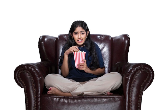 Mujer asiática comiendo palomitas mientras se sienta en el sofá con una expresión de miedo