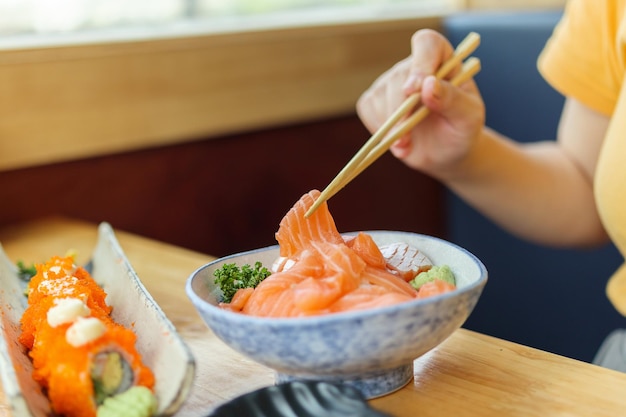 Mujer asiática comiendo sashimi de rebanada de salmón con arroz en restaurante japonés