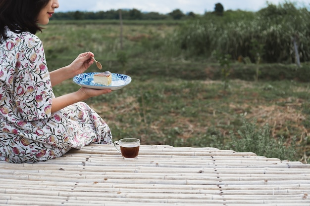 Mujer asiática comiendo tarta de queso con taza de café con vista al paisaje.