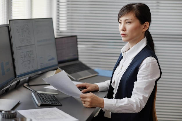 Mujer asiática como ingeniera que usa una computadora con planos en la oficina