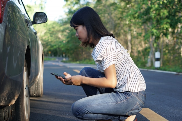 Mujer asiática Compruebe si hay coches rotos en las carreteras que rodean el bosque.