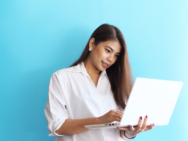 Mujer asiática con la computadora portátil en fondo azul