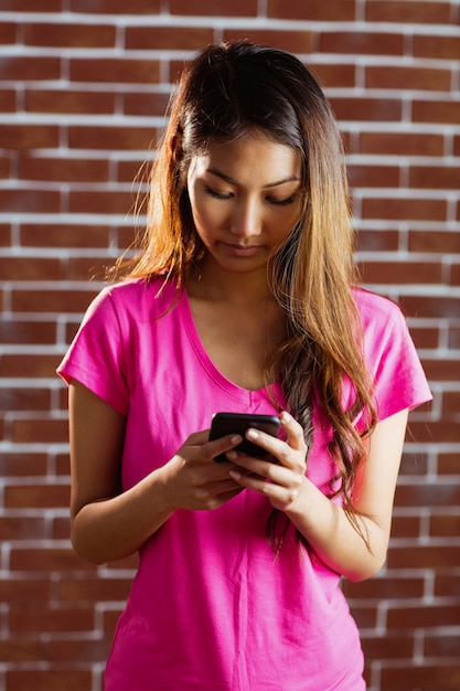 Mujer asiática concentrada con smartphone en pared de ladrillo