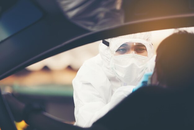 Mujer asiática conduce a través de la prueba de covid-19 con personal médico de ppe temperatura de prueba de covid mientras comprueba