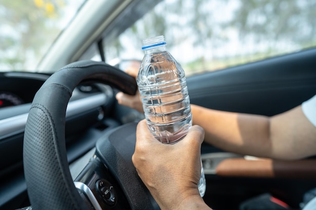 Mujer asiática conductora sosteniendo una botella para beber agua mientras conduce un automóvil Una botella plástica de agua caliente causa un incendio