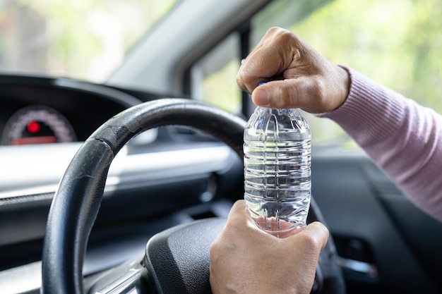 Mujer asiática conductora sosteniendo una botella para beber agua mientras conduce un automóvil Una botella plástica de agua caliente causa un incendio