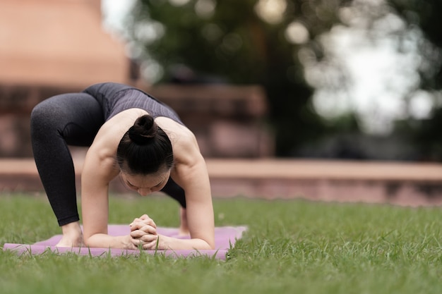 Una mujer asiática confiada en traje deportivo haciendo ejercicio de yoga al aire libre en el parque del patio trasero