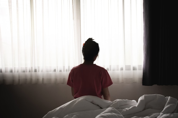 La mujer asiática deprimida se siente triste y sola sentada en la cama por la mañana.