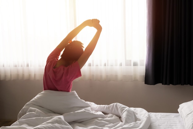 Foto mujer asiática despertando y estirando relajarse en la mañana del día soleado. concepto de feliz día de descanso.