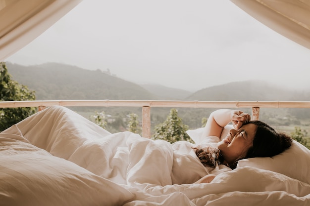 La mujer asiática despierta en la tienda y mirando la vista de la montaña en el tiempo de la puesta del sol,