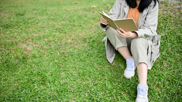 Una mujer asiática disfruta leyendo su libro mientras se relaja en el parque verde