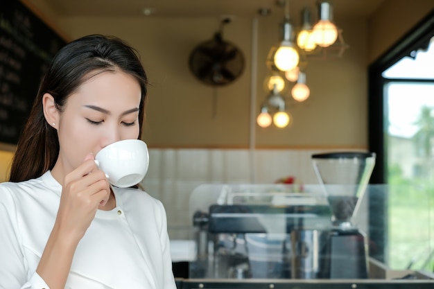 La mujer asiática disfruta con una taza de café en cafetería.