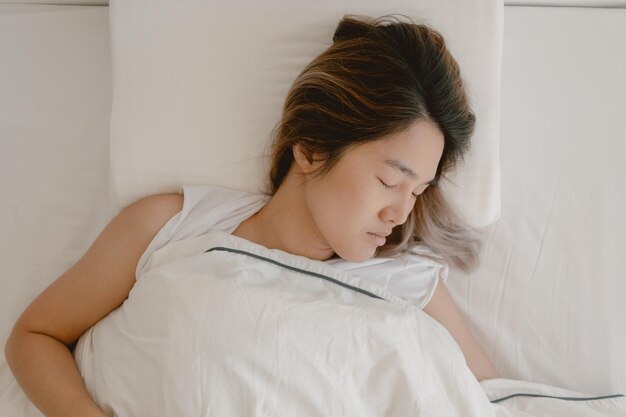 Mujer asiática durmiendo en una cama blanca duerme y descansa completamente hasta la mañana