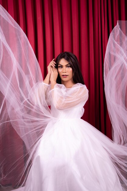 Mujer asiática elegante con un vestido de novia con tela voladora a su alrededor frente a la cortina roja