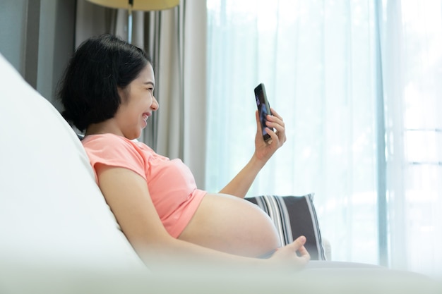 Mujer asiática embarazada haciendo videollamada en el teléfono inteligente en casa