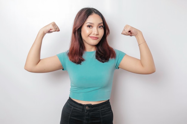 Mujer asiática emocionada con una camiseta azul que muestra un gesto fuerte levantando los brazos y los músculos sonriendo con orgullo