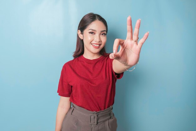 Mujer asiática emocionada con una camiseta roja dando un gesto de mano OK aislado por un fondo azul