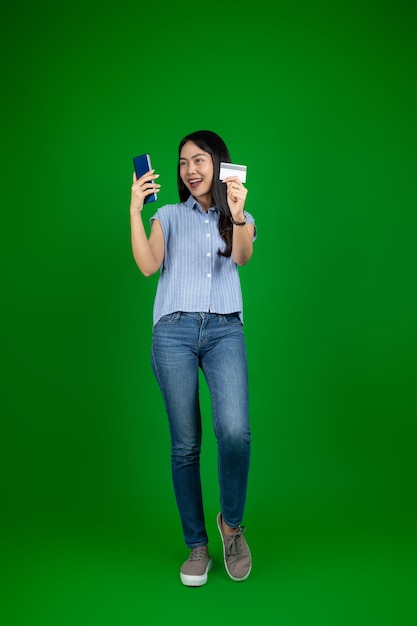 Mujer asiática emocionada que usa un teléfono móvil mientras sostiene la tarjeta del cajero automático de pie