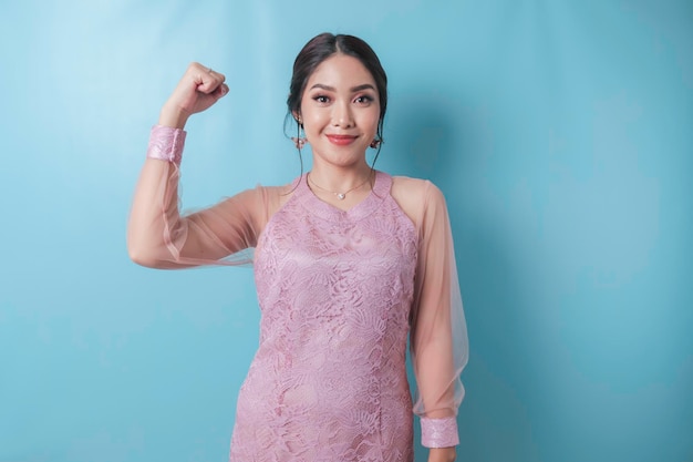 Mujer asiática emocionada con ropa moderna de kebaya mostrando un gesto fuerte levantando los brazos y los músculos sonriendo con orgullo