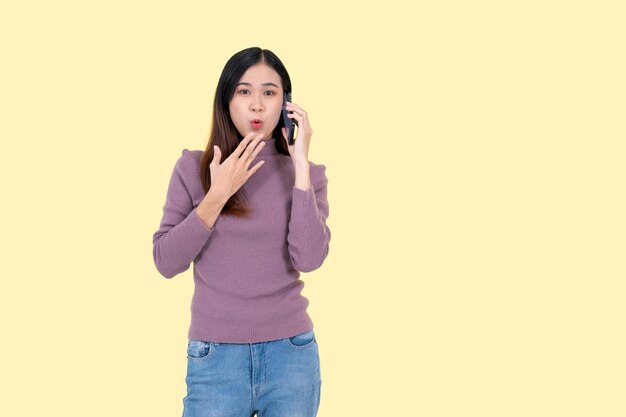 Una mujer asiática emocionada y sorprendida está hablando por teléfono con un fondo amarillo aislado