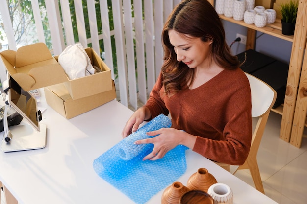 Mujer asiática empacando un jarrón con envoltura de burbujas de aire para un producto frágil antes de enviar el paquete