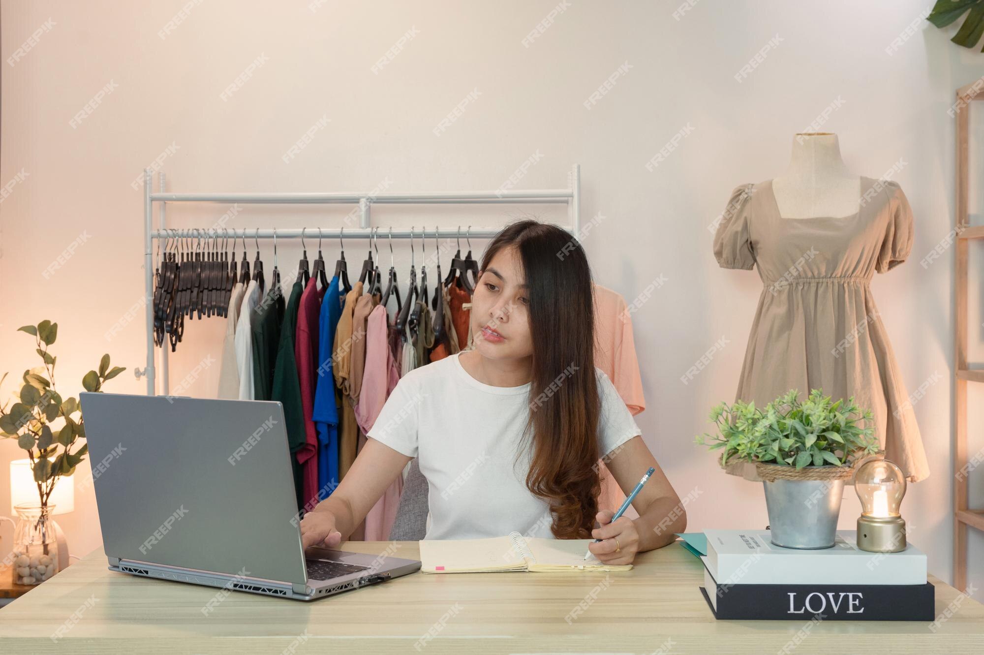 calor cuidadosamente Gallina Mujer asiática emprendedora de tienda de ropa en línea usando laptop y  tomando nota en el cuaderno en el escritorio en la oficina en casa | Foto  Premium