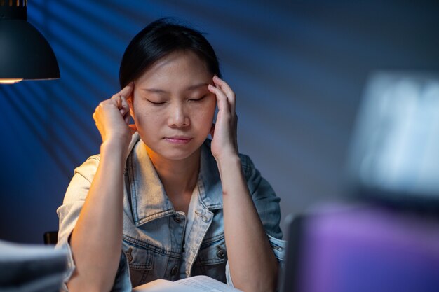 Foto mujer asiática escribiendo documentos en horas extras por la noche. plazo de trabajo en la oficina. dolor de cabeza de la muchacha del oficial y ocupado con su trabajo. infeliz y estrés.