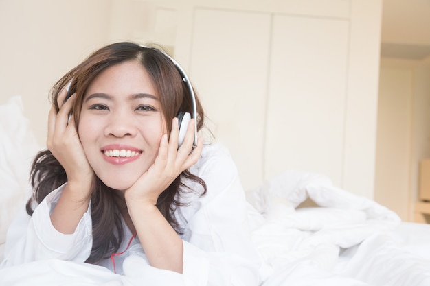 Mujer asiática escuchando música con auriculares en la cama