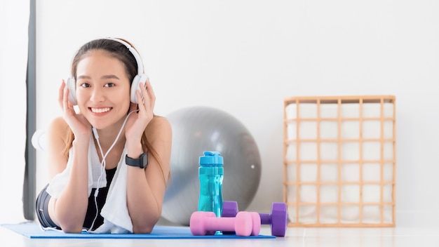 Mujer asiática escuchando música con auriculares después de jugar yoga y hacer ejercicio en casa de fondo con espacio de copia. Ejercicio para perder peso, aumentar la flexibilidad y apretar la forma.