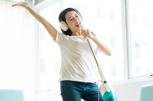 Mujer asiática escuchando música y bailando con una aspiradora