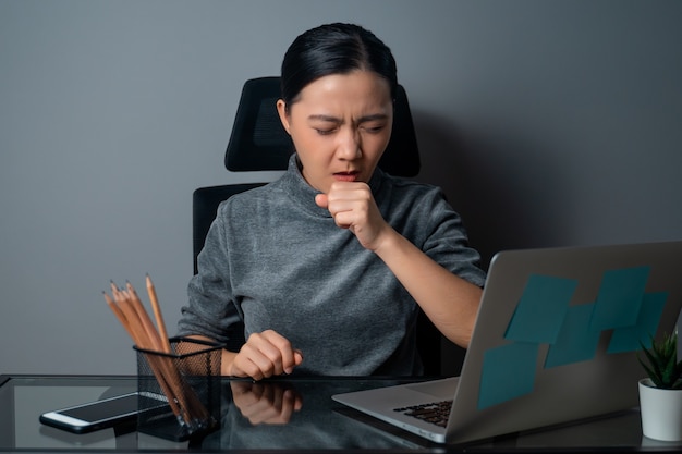 Mujer asiática estaba enferma de fiebre, trabajando en una computadora portátil en la oficina