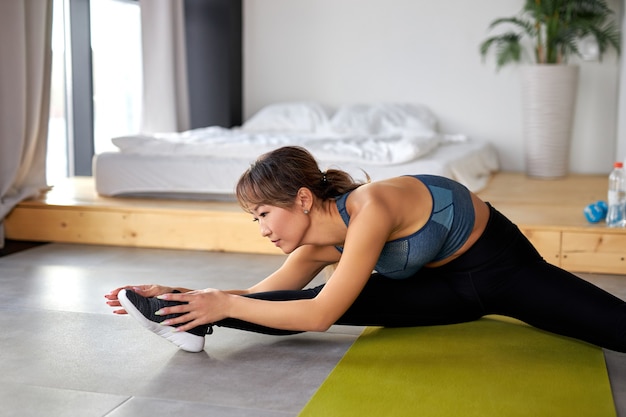 Mujer asiática estirando las piernas, haciendo ejercicios en la estera, entrenamiento. estilo de vida saludable y concepto deportivo