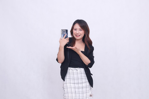 Mujer asiática con expresión alegre llevando un gadget de teléfono móvil mirando hacia atrás mientras presenta su mano